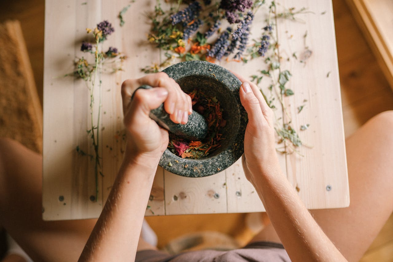 services-01 Top view of hands grinding dried herbs and petals with a mortar and pestle on a wooden table.