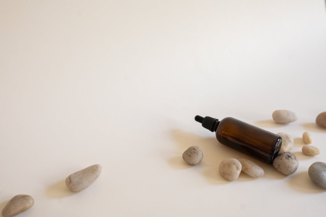 portfolio-02 Essential oil bottle surrounded by smooth stones on a white background, perfect for spa and wellness themes.