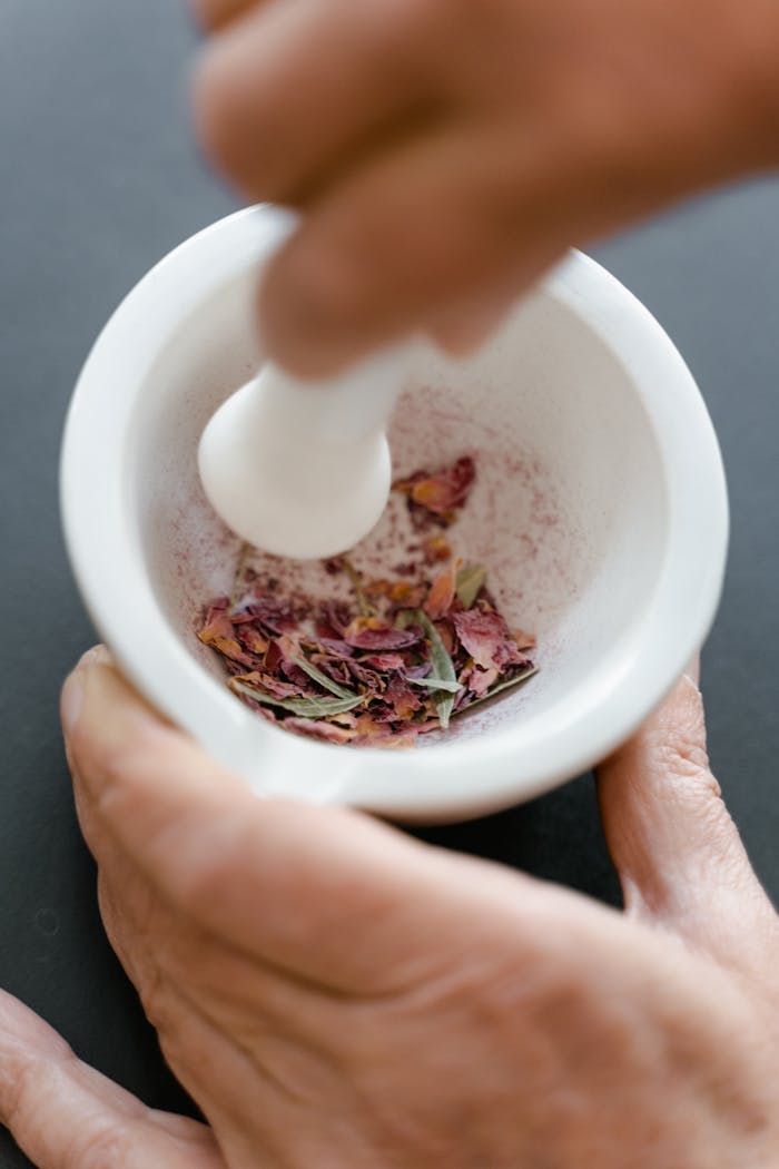 cta-02 A hand using a mortar and pestle to crush dried flower petals for body care products.